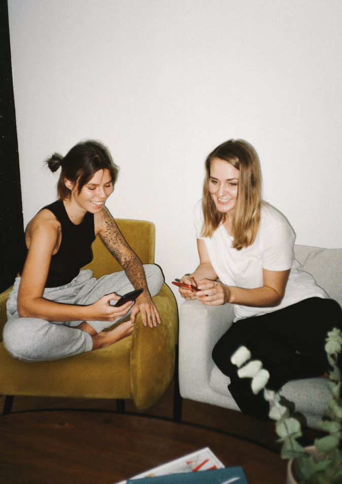 Twee vrouwen die samen op de bank een telefoon bekijken